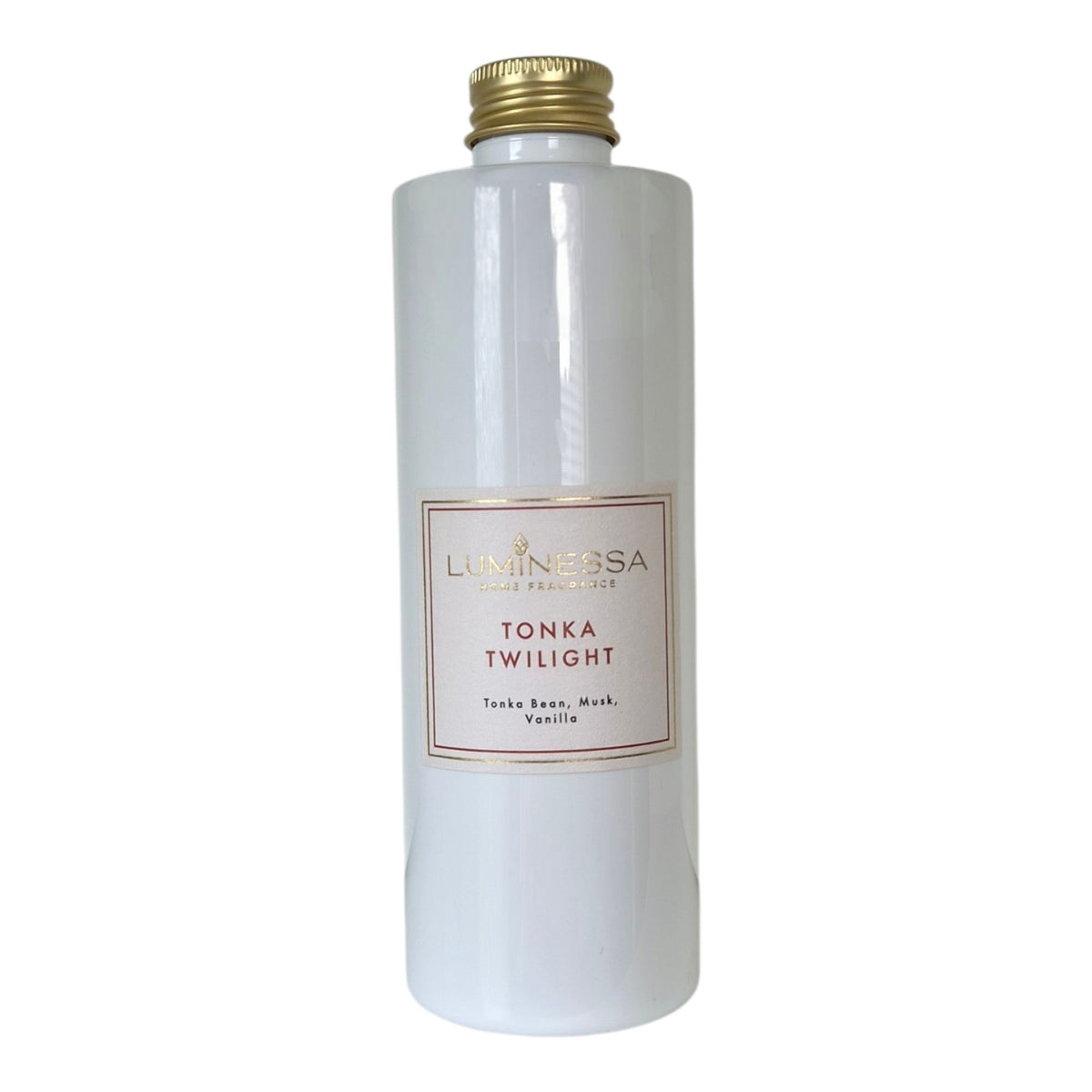 A tall, cylindrical white bottle of Luninessa Tonka Twilight with notes Tonka bean, Musk and Vanilla essence, featuring a gold ribbed cap and a cream-colored label with gold and red text.